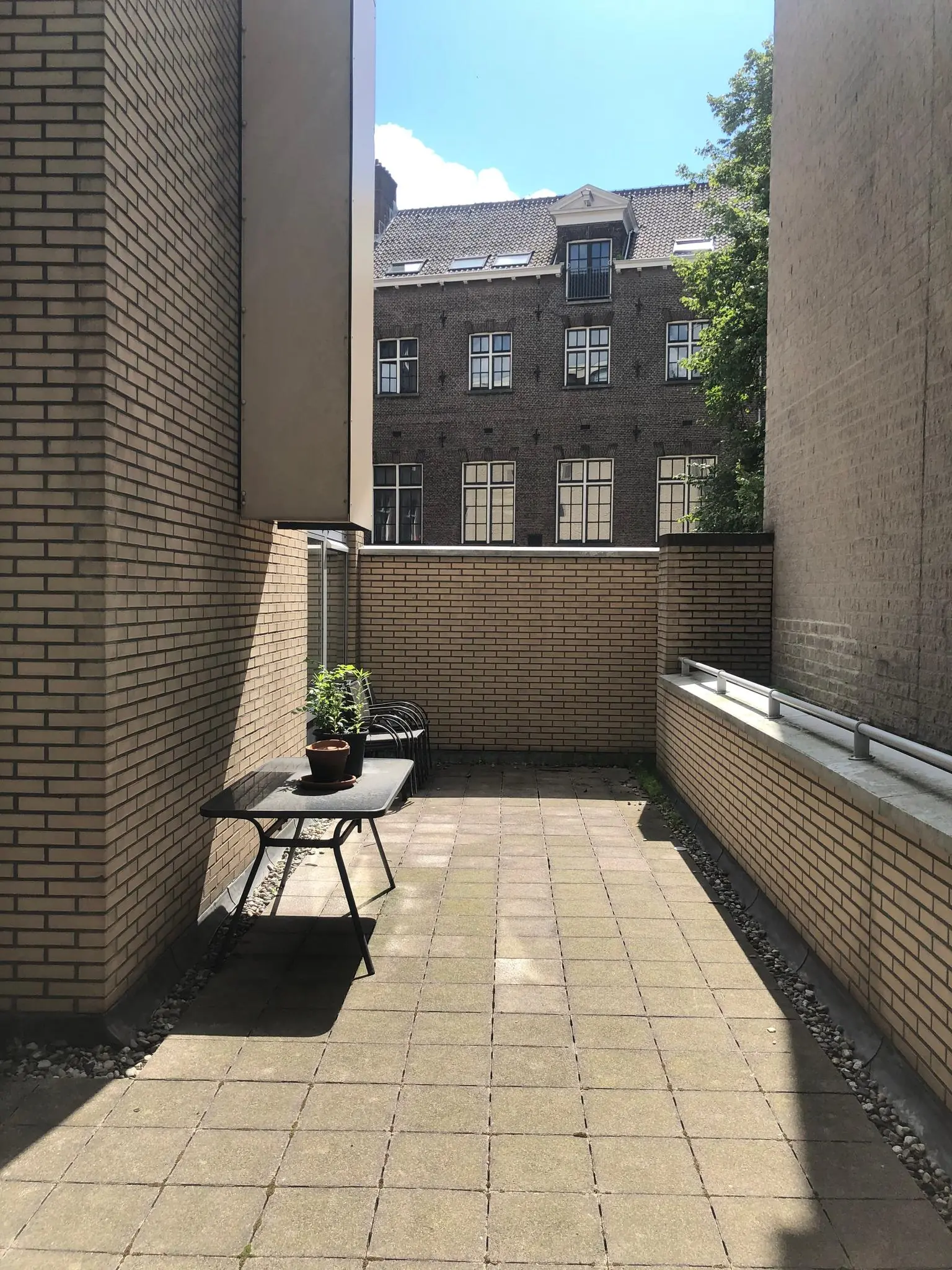 Binnenplaats met tegels en een zwarte tuintafel met planten, gelegen tussen gebouwen aan de Prins Hendrikkade.